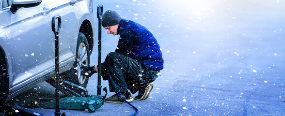Auto Mechanic car service, repair, maintenance and people concept - auto mechanic man with screwdriver changing tire at workshop over snow