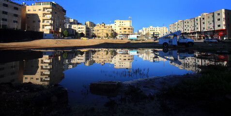 Reflection of buildings on the surface of a rainwater pond next to a street in Amman