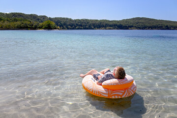 Boy relaxing floating on Lake McKenzie, Boorangoora, K'gari Fraser Island, holiday vacation travel destination, Queensland Australia