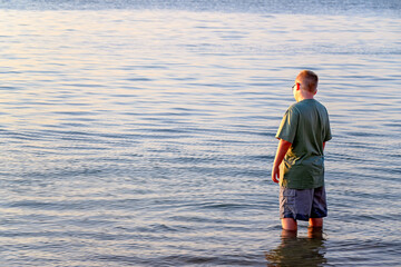 boy child standing in water ocean lake in late afternoon sunlight, summer family holiday vacation,...
