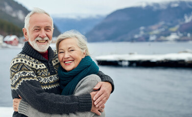 Fototapeta premium Portrait of happy scandinavian senior couple embracing each other in front of the nordic winter sea 