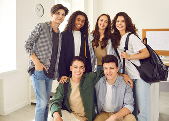 Group portrait of happy diverse high school friends in the classroom. Several teenage mixed race boys and girls in casual clothes smiling and looking at the camera all together