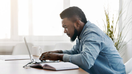 Responsible worker. Concentrated black employee working on laptop at workplace in modern office,...