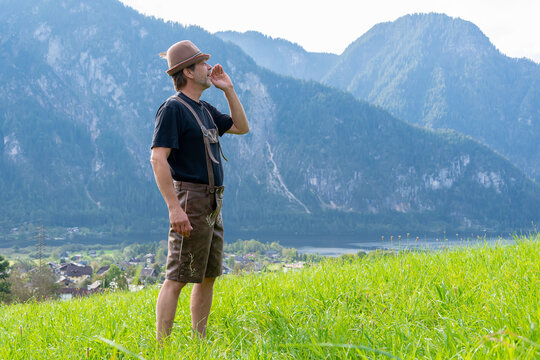 An elderly Tyrolean man, 50-55 years old, wearing traditional clothes, sings and shouts against the backdrop of a village surrounded by mountains, 