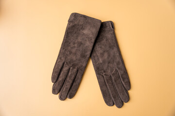 Womens dark brown gloves and baseball cap made of genuine suede on a peach fuzz background.