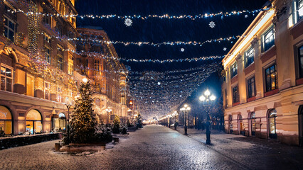 Fototapeta premium Evening street and trees decorated with luminous garlands. Christmas atmosphere with falling snow.
