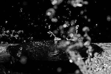 Dynamic splash of water creating droplets and ripples against a black background, captured in mid-motion to highlight the fluidity and abstract form © mikeosphoto