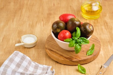 Different varieties of tomatoes in a ceramic bowl on a wooden background. Ingredients for salads.