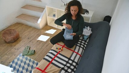 Woman folding clothes in cozy living room, organizing and tidying up, highlighting a minimalist lifestyle and home management.