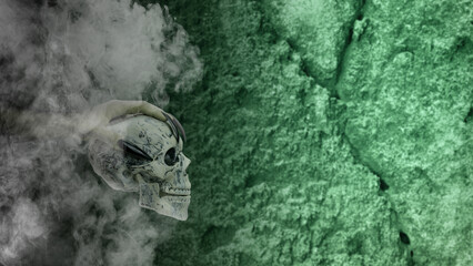 Witch hand with long black nail holding human head skull through smoke, gives the image a spooky and scary mood