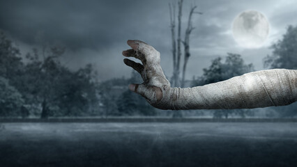 Mummy hand in bandages rising out with full moon background. Scene has dark and scary. The hand...