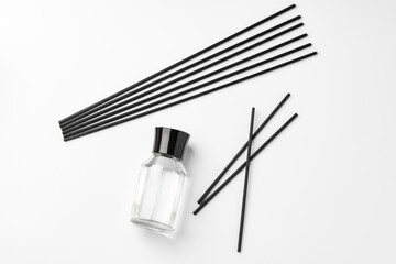 A minimalist display of essential oil and black diffuser sticks on a clean white background