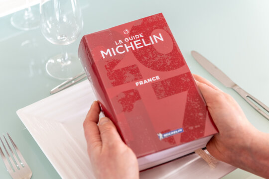 Paris, France - February 15, 2021 - Woman reading Red Michelin guide book which reviews restaurants.