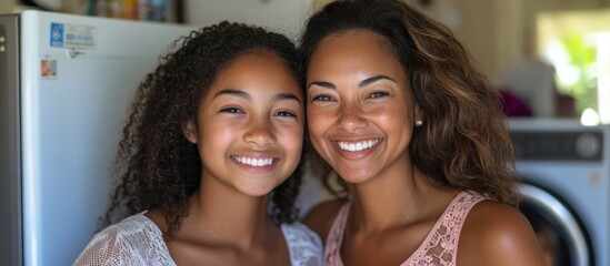 Fototapeta premium A mother and daughter smile happily at the camera in their kitchen.
