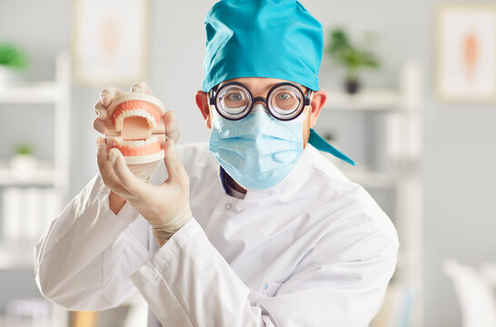 Close up portrait of funny man doctor dentist in blue mask and medical uniform looking at camera holding jaws in hands standing in dentistry clinic. Medicine and dental health care concept.