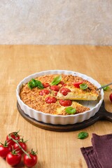 Frittata, egg casserole with cherry tomatoes, cheese and cornmeal in a light ceramic dish on a wooden background. Egg dishes.