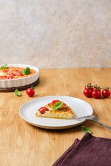 Frittata, egg casserole with cherry tomatoes, cheese and cornmeal in a light ceramic dish on a wooden background. Egg dishes.