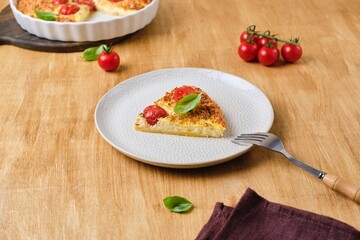 Frittata, egg casserole with cherry tomatoes, cheese and cornmeal in a light ceramic dish on a wooden background. Egg dishes.