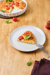 Frittata, egg casserole with cherry tomatoes, cheese and cornmeal in a light ceramic dish on a wooden background. Egg dishes.