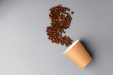 A coffee cup surrounded by roasted coffee beans on a gray surface