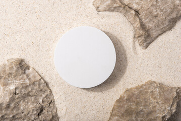 Natural cosmetic background for product presentation. Rocks and white podium on the sand. Top view.