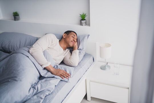 Photo of attractive young male lying bed sleeping dressed pajama wake up cozy day light home interior bedroom