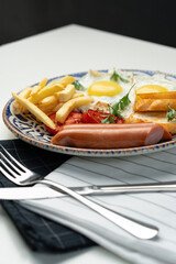 Breakfast plate with fried eggs, sausage, tomatoes, and fries served on a decorative blue plate