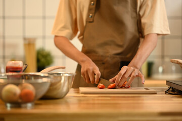 Young man preparing healthy meal, cutting tomatoes on a wooden cutting board