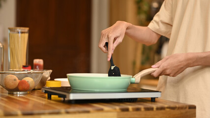 Close up shot of man stirring ingredients in frying pan with wooden spatula