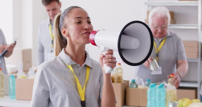 Young female volunteer megaphone speaking working in charitable food foundation, invite to make donation charity, donation stuff, basic need provisions, free meal, water for people in need, food bank
