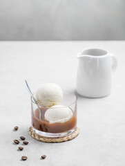 Affogato coffee with vanilla ice cream scoops and  espresso in a glass on a light  background with coffee beans and jug.