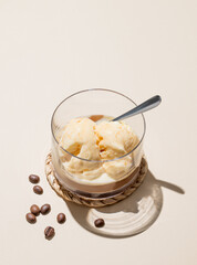 Affogato coffee with vanilla ice cream scoops  and espresso in a glass on a light background with coffee beans, spoon  and shadow.