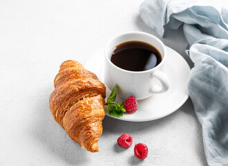 Cup of espresso coffee and croissant with fresh raspberries and mint on a plate on a white texture  background with morning light and napkin.