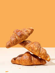 Stack of fresh croissants on yellow and orange background. Creative trendy layout and concept of healthy food or french breakfast