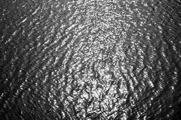 Monochrome ripples of water reflecting sunlight, creating a mesmerizing texture and abstract pattern in nature.