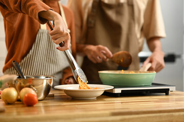 Young couple cooking spaghetti in a cozy kitchen. People, food and domestic life concept