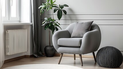 Interior of beautiful living room with cushion, stylish grey armchair and pouf near white wall