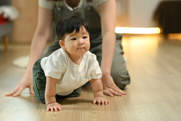 Little baby boy learning to crawl with supportive mother closely watching from behind. Childhood and development concept