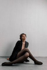 Woman with short hair sits elegantly on the floor, her legs extended, dressed in a black outfit....
