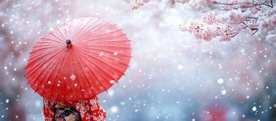 Woman holding a red umbrella in the snow with cherry blossoms behind her.