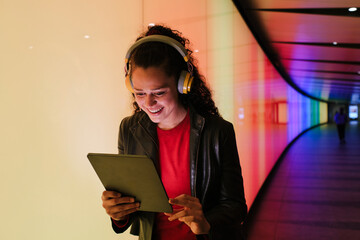 Young woman using tablet and wearing headphones in colorful tunnel