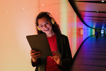 Young woman wearing headphones using tablet in colorful tunnel at night
