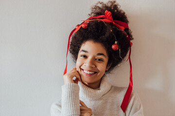 Close-up of young African with curly hairstyle decorated with red ribbon, garland and Christmas balls