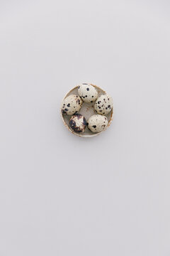 Five quail eggs in a small bowl on a light grey table top.
