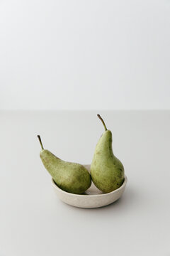Two pears in a beige ceramic bowl on a light grey table top.