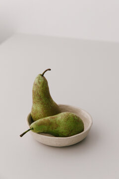 Two pears in a beige ceramic bowl on a light grey table top.