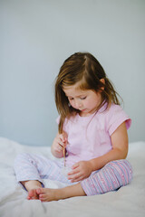 Fototapeta premium A girl child eats ice cream sitting on the bed. Rejoices, grimaces, enjoys. Holiday, weekend, home