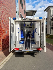 An ambulance with its rear door open and a patient stretcher extended stands outside a hospital in Germany waiting for a patient. Vertical format.