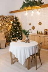 Round table with a white tablecloth and a vase with fir branches stand in the kitchen near the Christmas tree