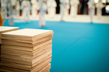 Blurry Taekwondo students in white uniform practice on training mats with stack of wooden boards in Texas, breaking boards for punch, kick grading testing, thin pine plywood square sheets